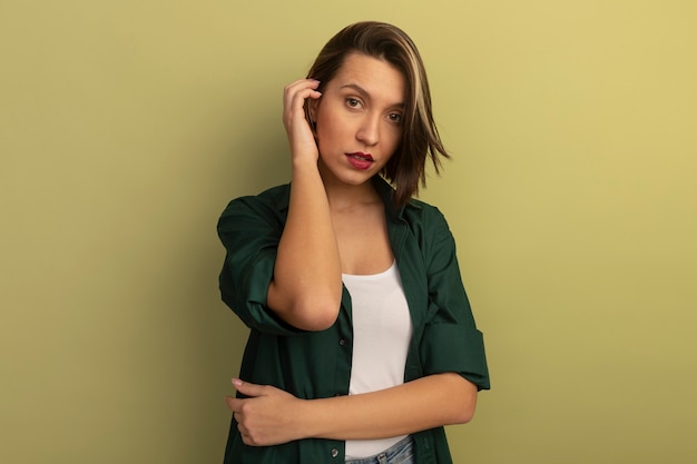 Confident pretty woman holds hand close to head isolated on olive green wall