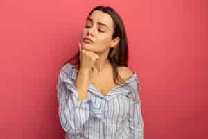 Free photo confident pretty woman puts hand on chin and looks at side isolated on pink wall