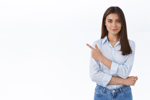 Confident professional young woman in blue blouse pointing finger upper left corner and looking at camera persuade customer make right choice and sign deal with her company white background