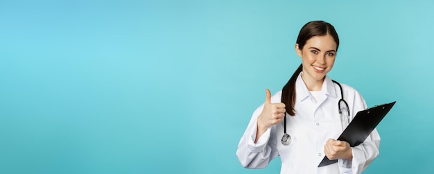 Free Photo confident smiling doctor woman physician showing thumbs up holding clipboard appointment in hospital