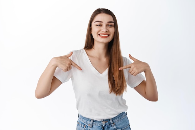 Confident smiling girl pointing at herself showing center logo selfpromoting demonstrate promotional text standing over white background