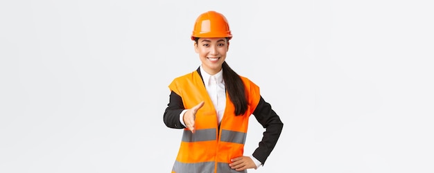 Confident successful female architect leader of construction in safety helmet reflective jacket extand hand for handshake greeting business partners at building area standing white background