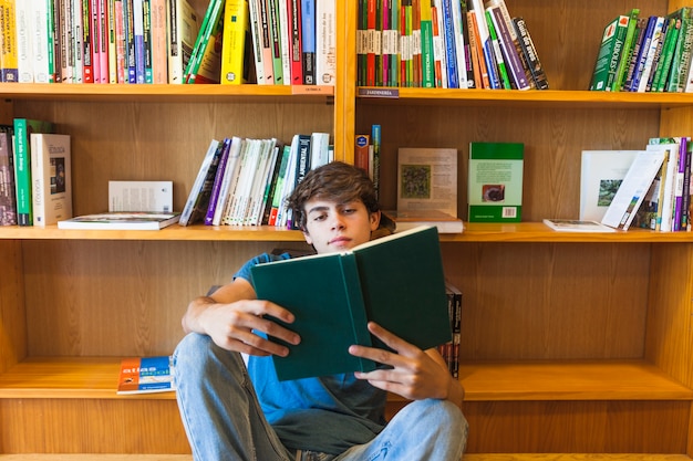 Confident teenager reading on floor near bookcase