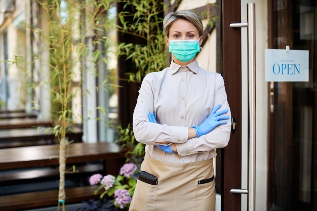 Confident waitress with protective face mask and gloves reopening cafe during coronavirus epidemic