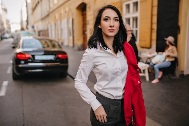 Free Photo confident woman with black hair posing on the street with car on wall