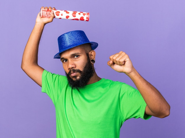 Confident young afro-american guy wearing party hat holding confetti cannon showing yes gesture 