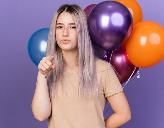 Confident young beautiful girl standing in front balloons showing you gesture 