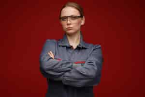 Free photo confident young blonde female engineer wearing uniform and safety glasses standing with closed posture