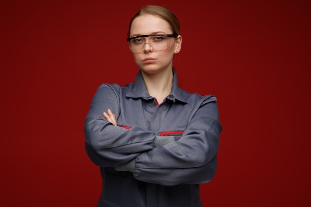 Free Photo confident young blonde female engineer wearing uniform and safety glasses standing with closed posture 