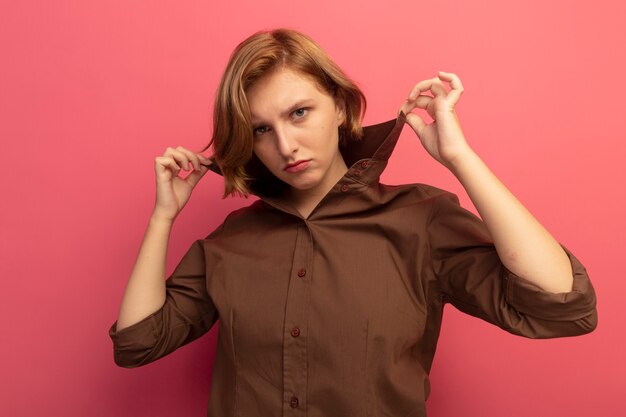 Confident young blonde girl grabbing collar of shirt 