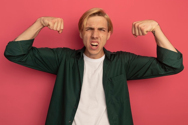 Free Photo confident young blonde guy wearing green t-shirt doing strong gesture isolated on pink