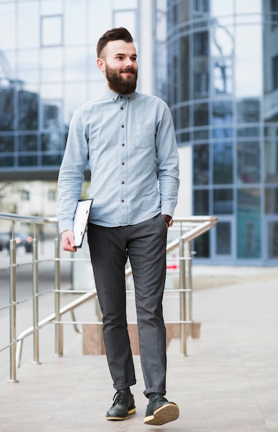 Free photo confident young businessman walking in front of corporate building