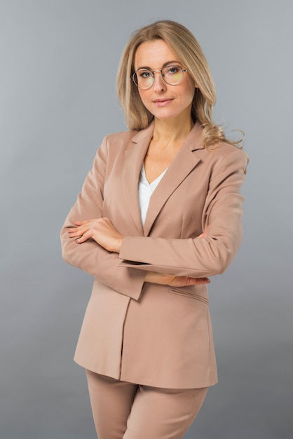 Free Photo confident young businesswoman standing with her arm crossed against gray backdrop