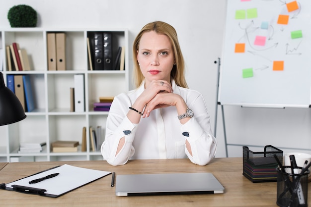 Confident young businesswoman with laptop on table in the office