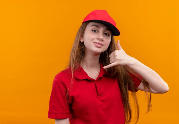 Confident young delivery girl in red uniform doing call gesture on isolated orange space with copy space