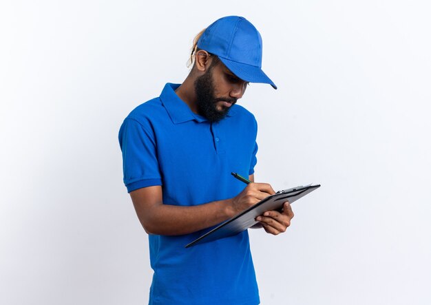 confident young delivery man writing something on clipboard isolated on white wall with copy space