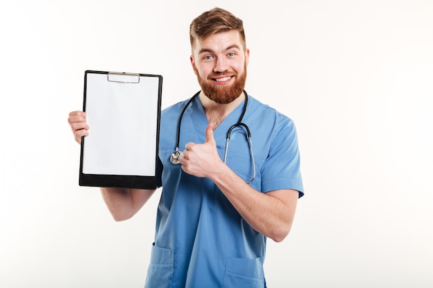 Confident young doctor holding clipboard and giving thumb up