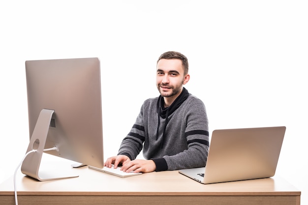 Confident young entrepreneur sitting at the table with laptop and pc, looking at camera isolated on white