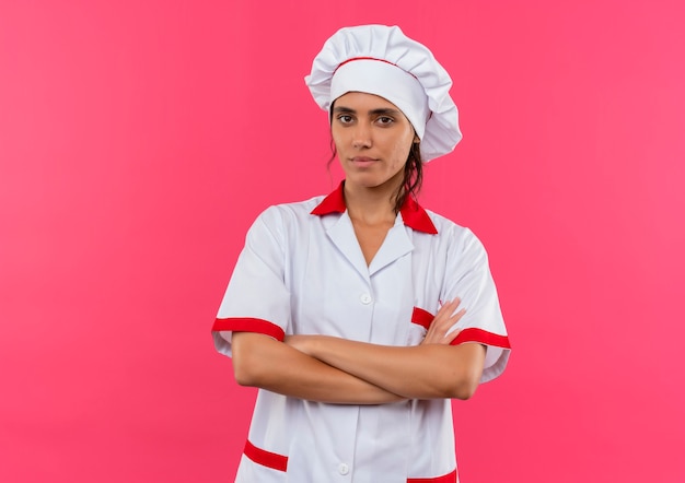 Confident young female cook wearing chef uniform crossing hands on isolated pink wall with copy space