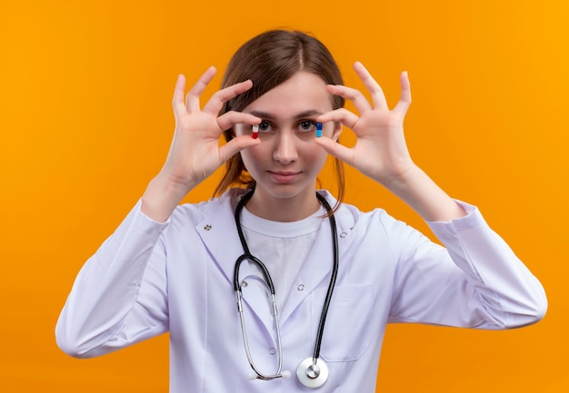 Free Photo confident young female doctor wearing medical robe and stethoscope showing medical capsules on isolated orange space