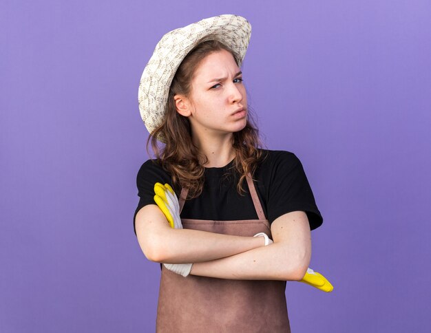 Confident young female gardener wearing gardening hat with gloves crossing hands 