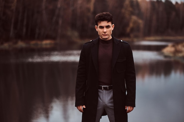 Free Photo a confident young handsome man standing near a lake in the autumn forest.