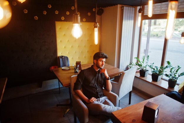 Free Photo confident young indian man in black shirt sitting at cafe