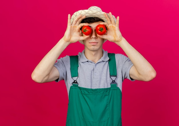 Free Photo confident young male gardener wearing gardening hat covers eyes with tomatoes 