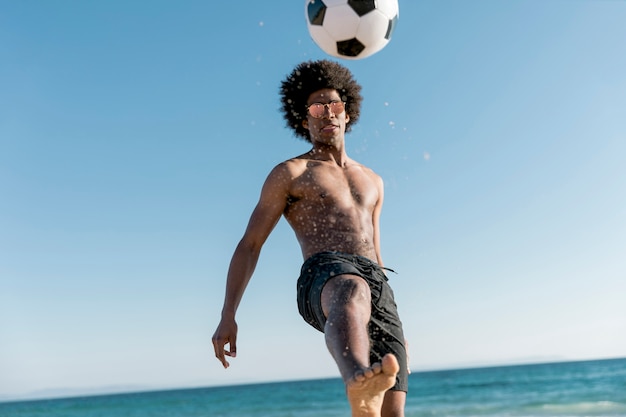 Free photo confident young male kicking ball on seashore