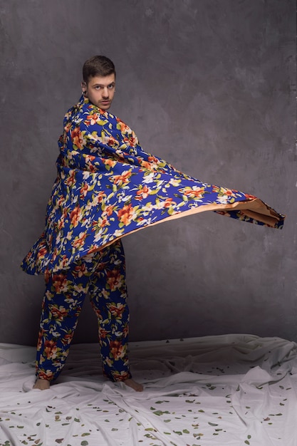 Confident young man blowing his floral drape against grey wall