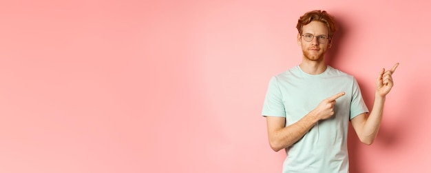 Free photo confident young man with ginger hair and beard smiling pleased and pointing fingers at upper right c