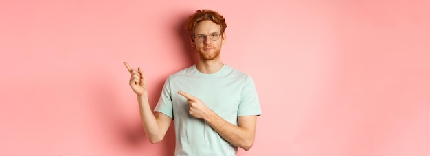 Free photo confident young man with ginger hair and beard smiling pleased and pointing fingers at upper right c