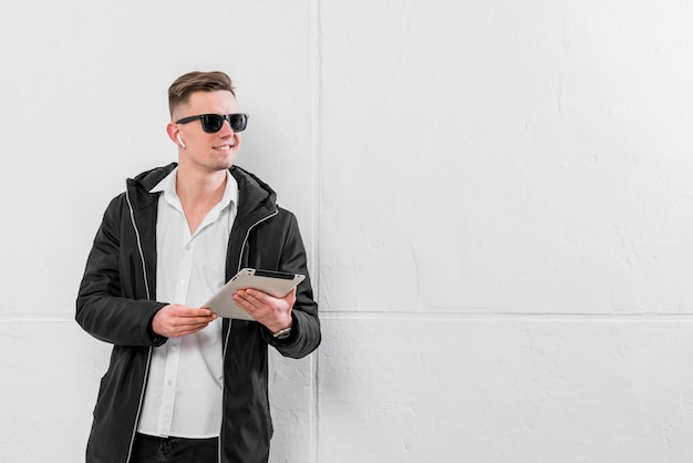 Free Photo confident young man with wireless earphone on his ear holding digital tablet in hand looking away