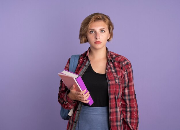 Confident young slavic student girl wearing backpack holds book and notebook 