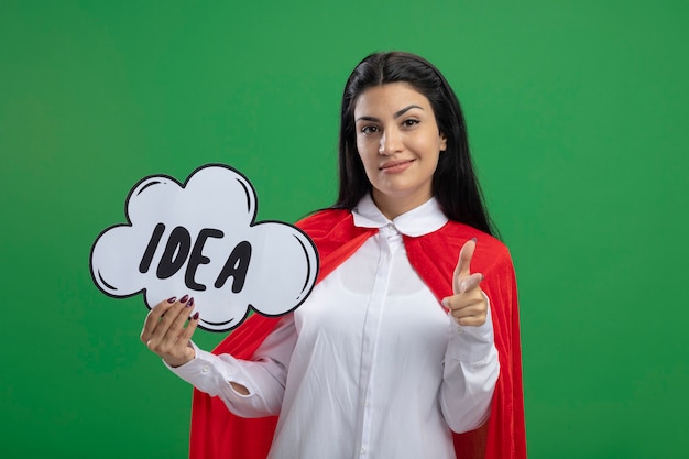 Free photo confident young superwoman holding idea bubble and pointing her index finger to audience looking at front isolated on green wall