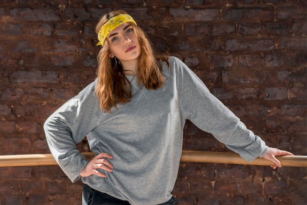 Confident young woman standing in front of brick wall leaning on barre