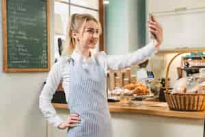 Free photo confident young woman taking selfie from mobile phone in her coffee shop