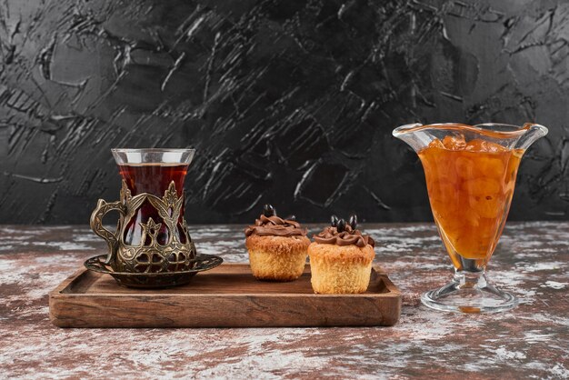 Confiture, muffins and a glass of tea on a wooden board.