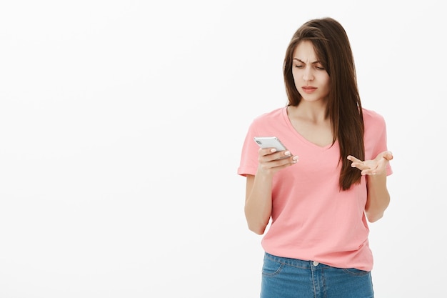 Confused brunette woman posing in the studio with her phone