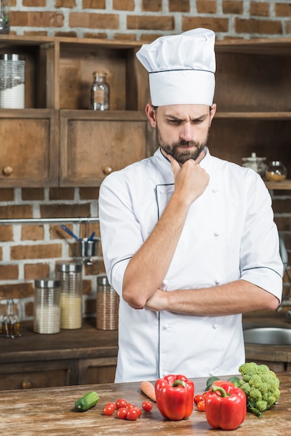 Free photo confused cook standing behind the kitchen counter with colorful vegetables