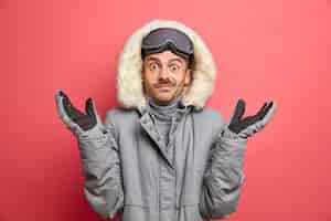 Free photo confused hesitant adult european man shrugs shoulders with doubt wears winter outerwear and gloves goes skiing during winter time.