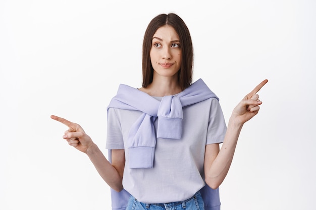 Free Photo confused, indecisive brunette girl cant make her choice, pointing sideways and looking at left side, choosing, deciding between two ways, standing over white wall