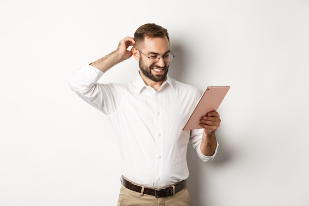 Confused male manager looking puzzled at digital tablet, scratching head doubtful, standing  