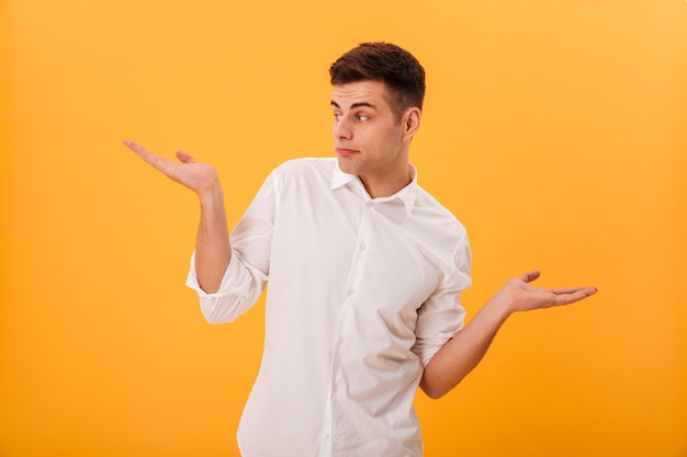 Free photo confused man in white shirt shrugs his shoulder and looking away