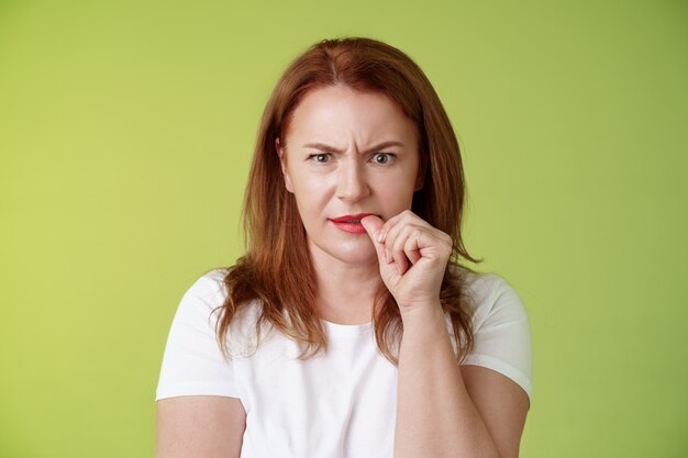 Confused puzzled redhead middleaged mother perplexed look troubled solving troublesome situation pondering solution biting thumb nail frowning intense stare camera thinking thoughtfully