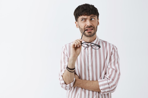 Confused and puzzled stylish bearded guy posing against the white wall with glasses