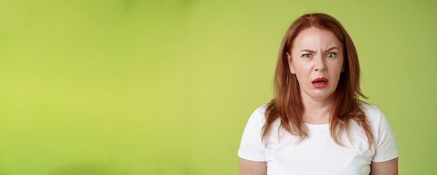 Free photo confused shocked gasping middleaged redhead woman cringe frustrated puzzled open mouth speechless freak out strange shocking scene stand green background perplexed disappointed