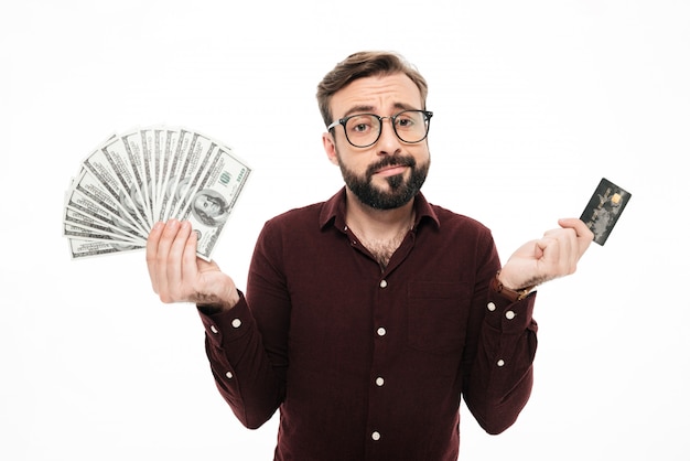 Confused thinking young man holding money and credit card.