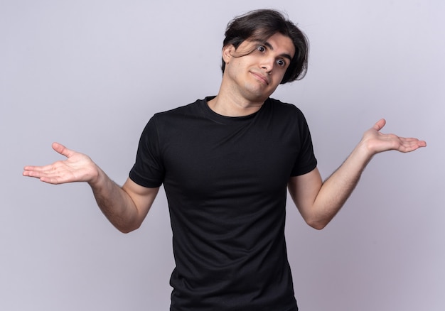 Confused tilting head young handsome guy wearing black t-shirt spreading hands isolated on white wall