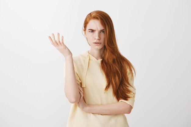 Confused and upset redhead girl raising hand up and look frustrated